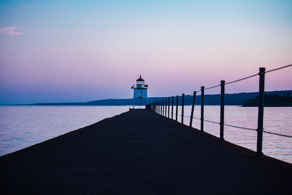 Lighthouse at the end of walkway in front of a sunset