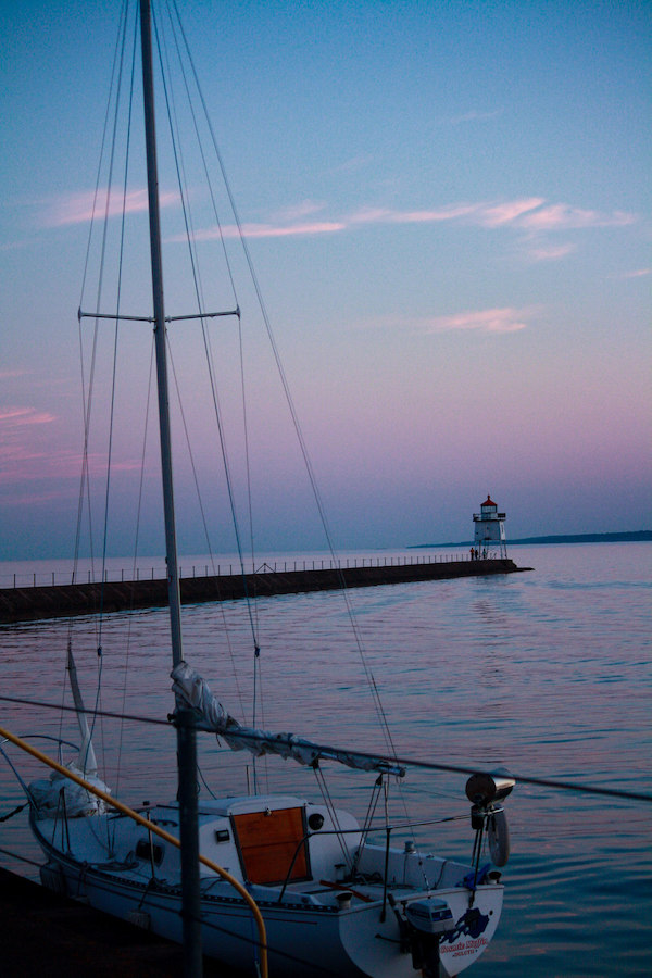 Sailboat with a lighthouse in the background at sunset