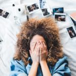 Woman lying on a bed with polaroids scattered around her