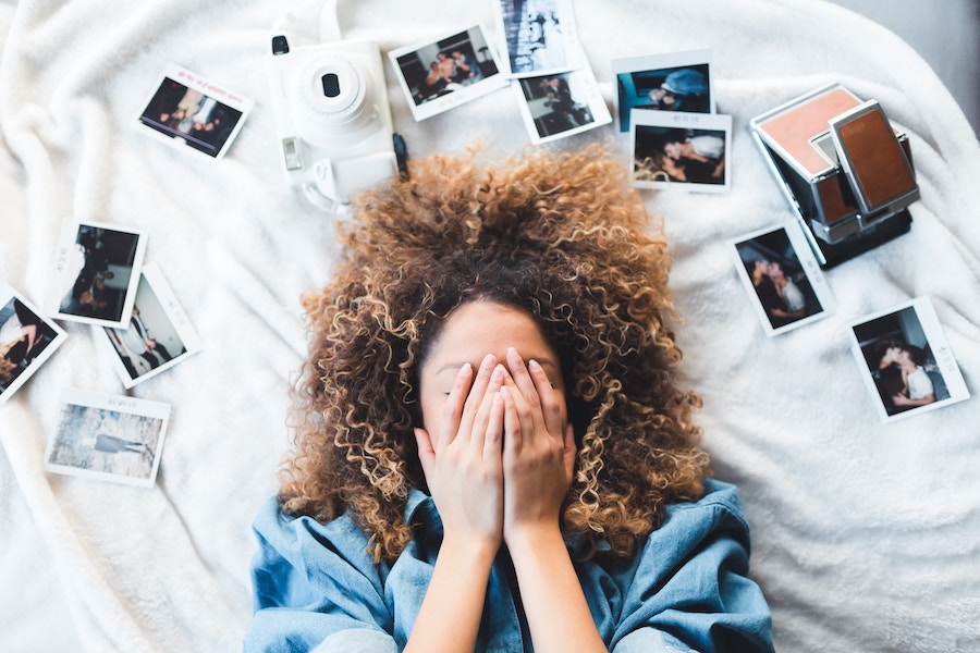 Woman lying on a bed with polaroids scattered around her