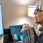 Woman with glasses and holding a mug looking over pie graphs and reports on her desktop