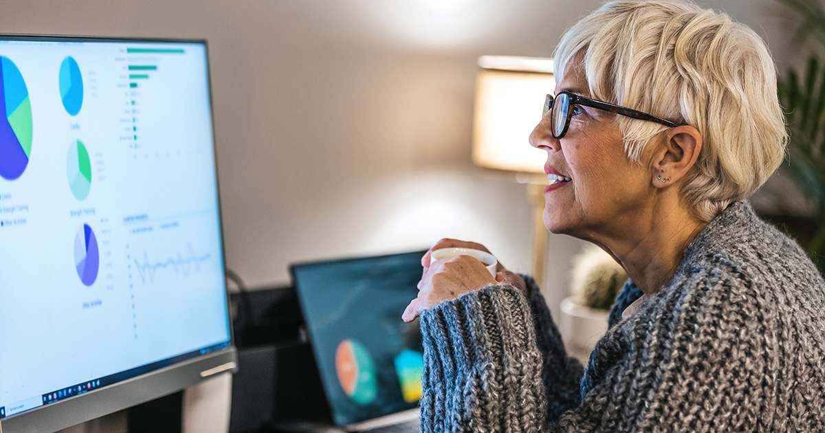 Woman with glasses and holding a mug looking over pie graphs and reports on her desktop